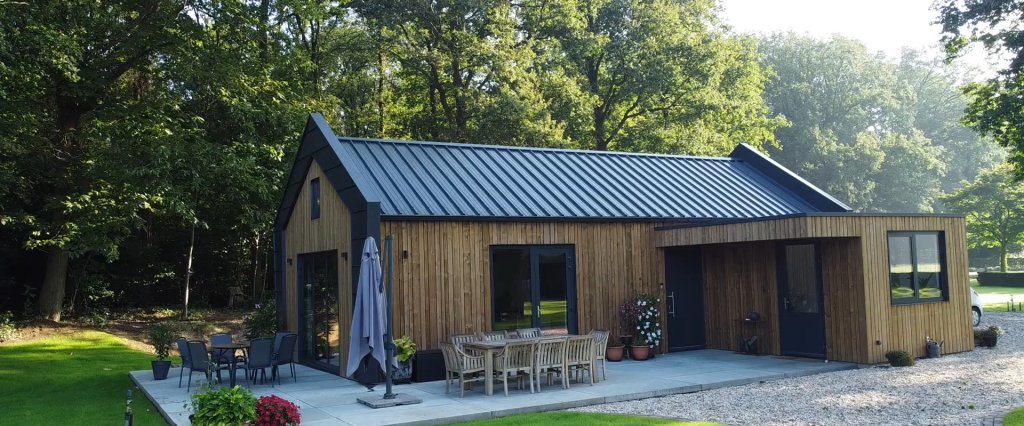 Houten familiewoning met terras en tuinmeubilair tussen de bomen.